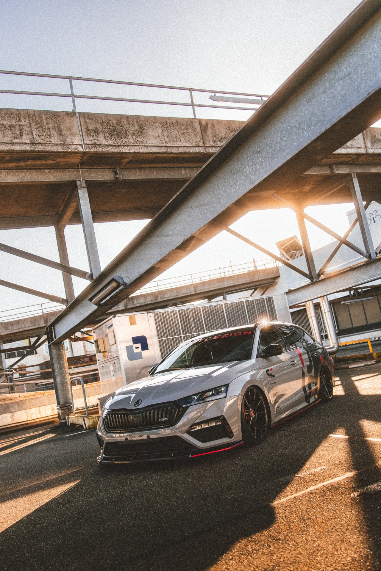 Sherin and Chris’s grey, black and red Škoda Octavia RS in warm sunlight beneath an industrial structure